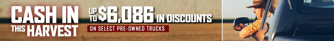A person driving a truck through a farm field is shown on the right. The left side has text: Cash in this harvest and Up to $6,086 in discounts on select pre-owned trucks.