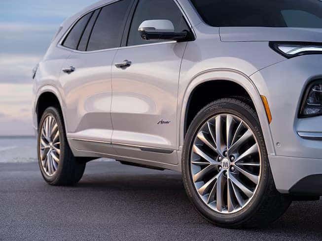 Silver SUV with large alloy wheels parked on a paved surface. The background shows a clear sky, and the vehicles nameplate is visible on the side. The focus is on the vehicles front wheel and side profile.
