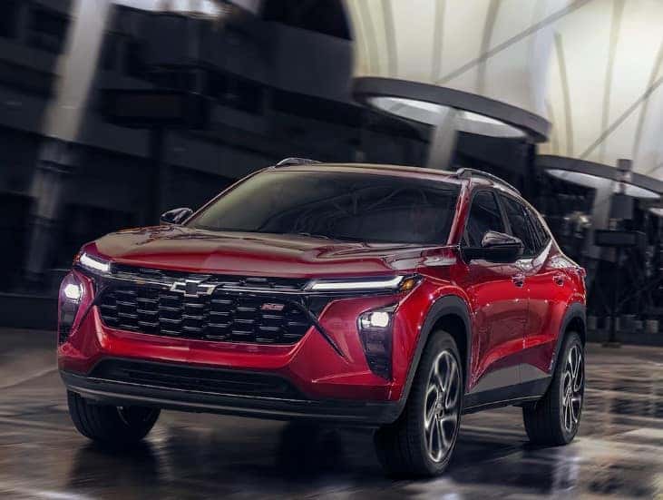 Red SUV with a sleek design parked indoors. The vehicle has prominent headlights and a bold front grille. The setting features a modern and spacious environment with architectural elements in the background.