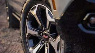 Close-up of a cars front wheel featuring a stylish, multi-spoke alloy rim with a GMC logo at the center. The tire is slightly dusty, suggesting off-road use. The cars body is partially visible, revealing a rugged design.