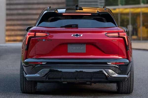 Red Chevrolet car viewed from the rear, displaying the brands logo and sleek taillight design. The car is parked on a paved surface with blurred buildings in the background.