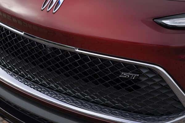 Close-up of a cars front grille with a diamond pattern in black, featuring a metallic ST badge on the right side. The surrounding body is a glossy red color, and a portion of the car emblem is visible at the top.
