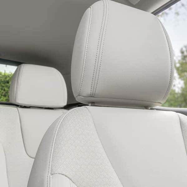 Close-up of a cars interior showcasing light-colored leather seats and headrests. Soft natural light highlights the stitching details. A window reveals a blurred view of greenery outside.