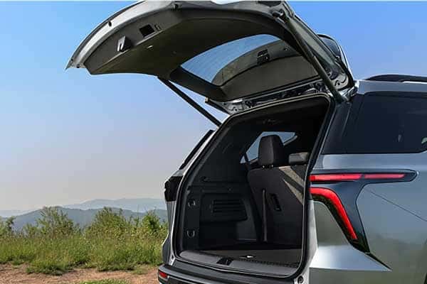 An SUV with its tailgate open, showing a spacious cargo area. The vehicle is parked in a grassy area with rolling hills and a clear blue sky in the background.