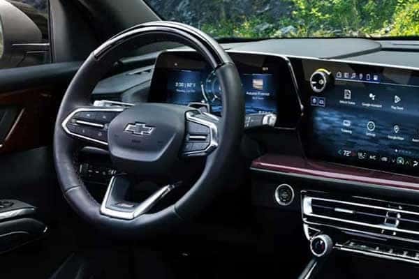 Close-up of a car interior showing a steering wheel with a Chevrolet logo, a digital dashboard displaying controls and information, and sleek modern design elements with a mix of black and brushed chrome details.