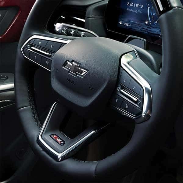 Close-up of a car steering wheel featuring a Chevrolet logo in the center. The wheel has integrated buttons for controls. The dashboard display in the background shows the time and date as 2:30 PM, July 17th.
