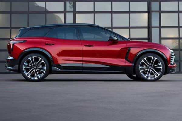 A sleek, red SUV with black trim and polished alloy wheels is parked in front of a modern glass-paneled building. The cars design features smooth curves and a stylish, aerodynamic profile.