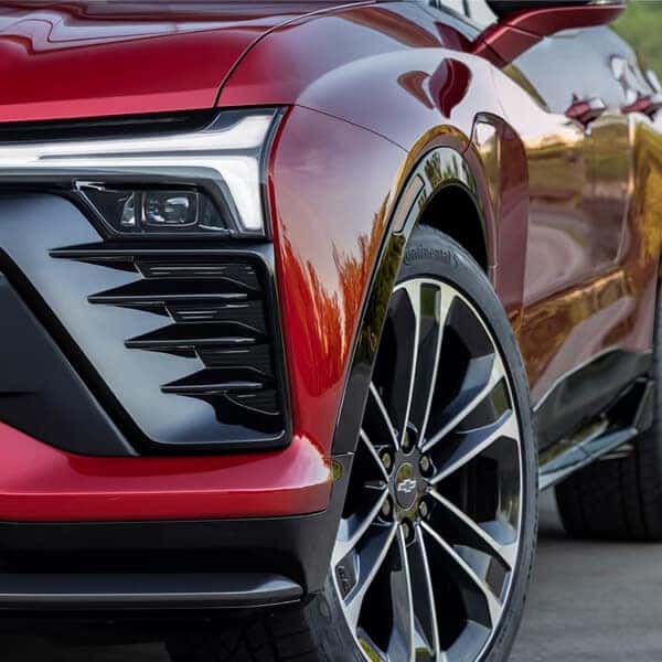 Close-up of a red sports cars front section, showcasing sleek LED headlights, a glossy finish, and shiny alloy wheels. The angle highlights the cars dynamic design and modern features.