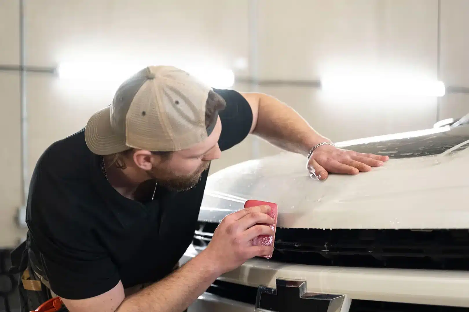 Technician applying car paint protection film in a workshop, blurring in the background.