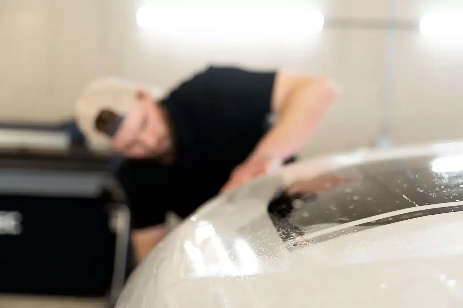 Technician applying car paint protection film in a workshop, blurring in the background.