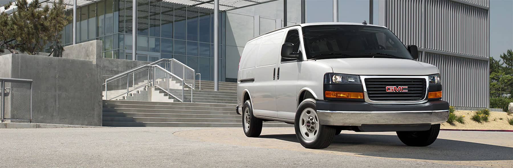 White GMC cargo van parked outside a modern building, emphasizing utility and commercial use.