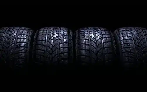 Four winter tires with detailed treads, illuminated against a dark background.