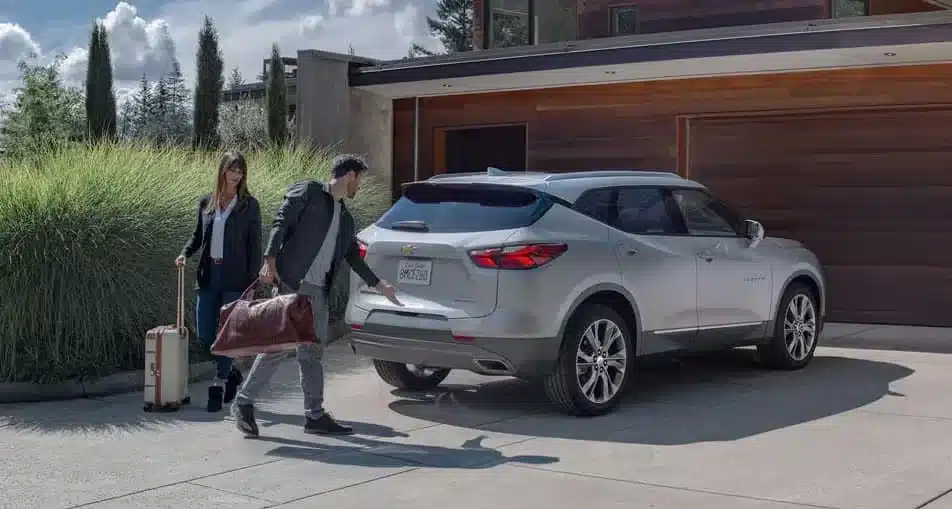 Couple loading luggage into a silver SUV in a modern driveway, highlighting travel and convenience.