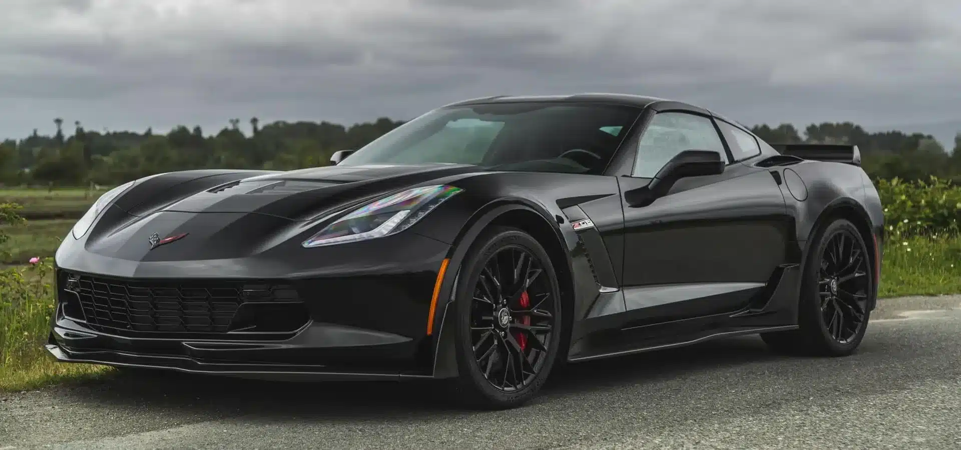 Sleek black sports car on a scenic road under cloudy skies, showcasing luxury design.