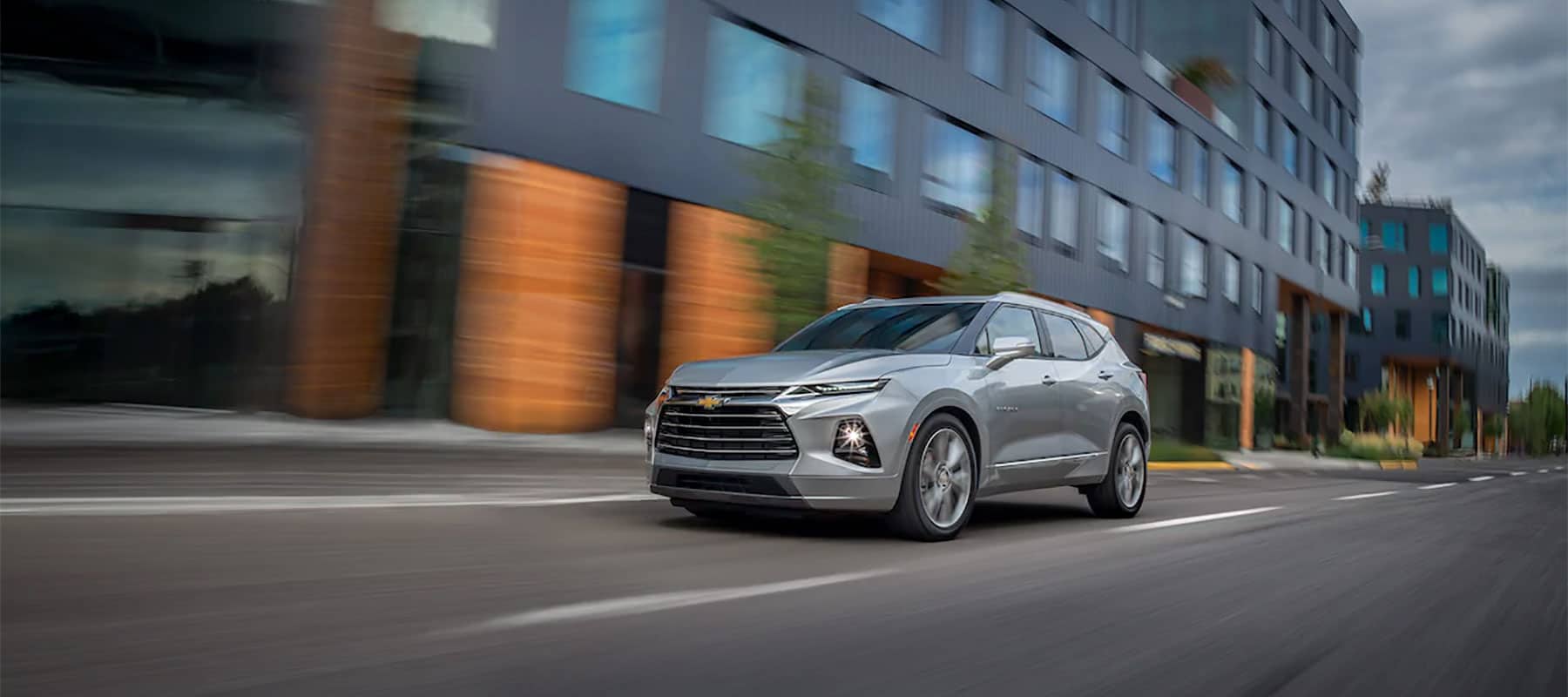 Silver SUV driving in an urban setting, showcasing sleek design and modern architecture.