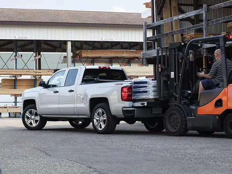 Forklift loading supplies onto a white pickup truck at a lumber yard, showcasing efficient material handling.