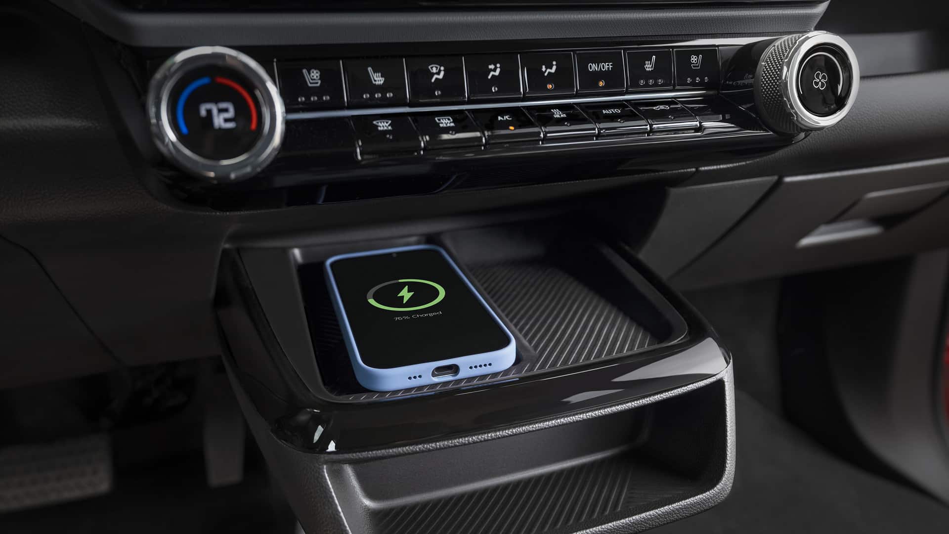 Smartphone wirelessly charging on a tray in a car, with dashboard buttons and temperature display.