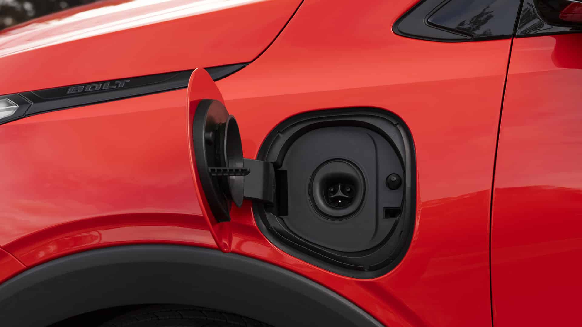 Close-up of a red electric car's open charging port with "Bolt" branding.