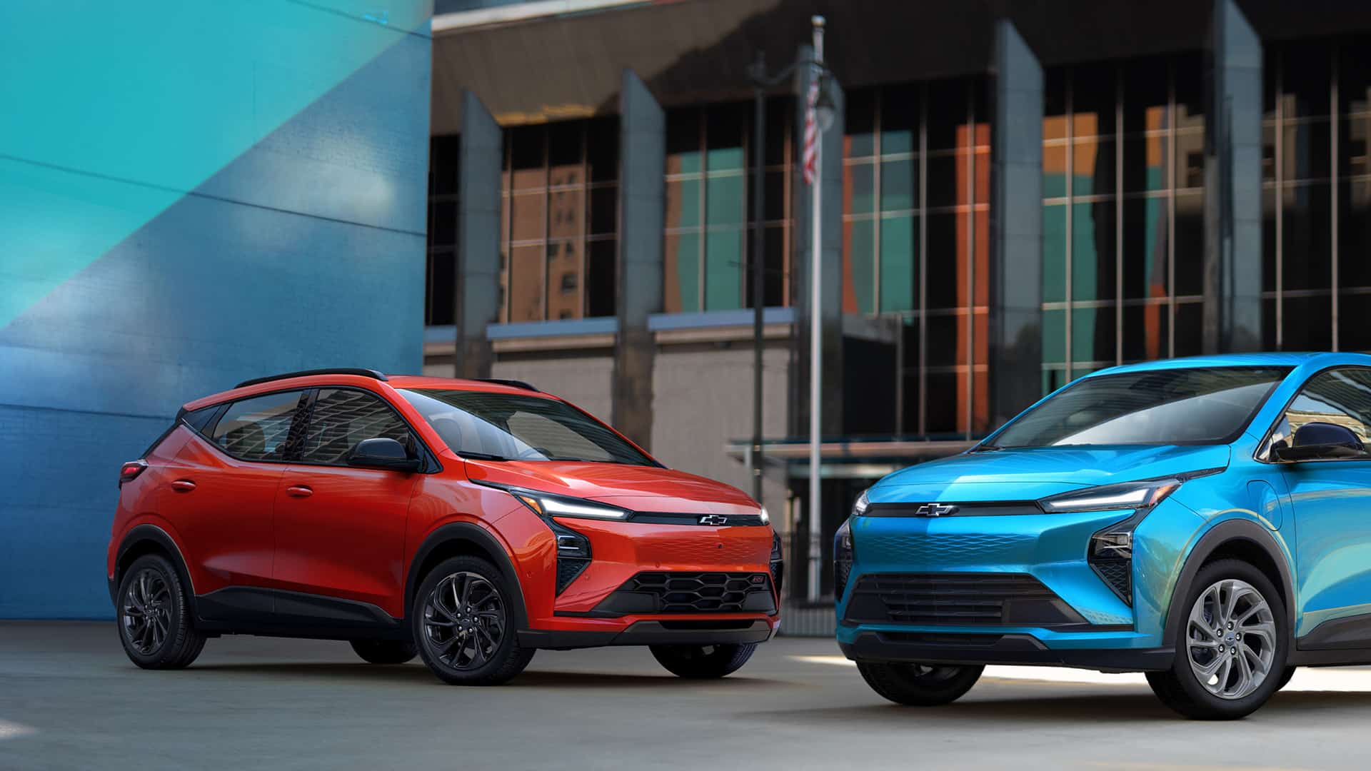 Red and blue electric SUVs parked in an urban setting with modern architecture.