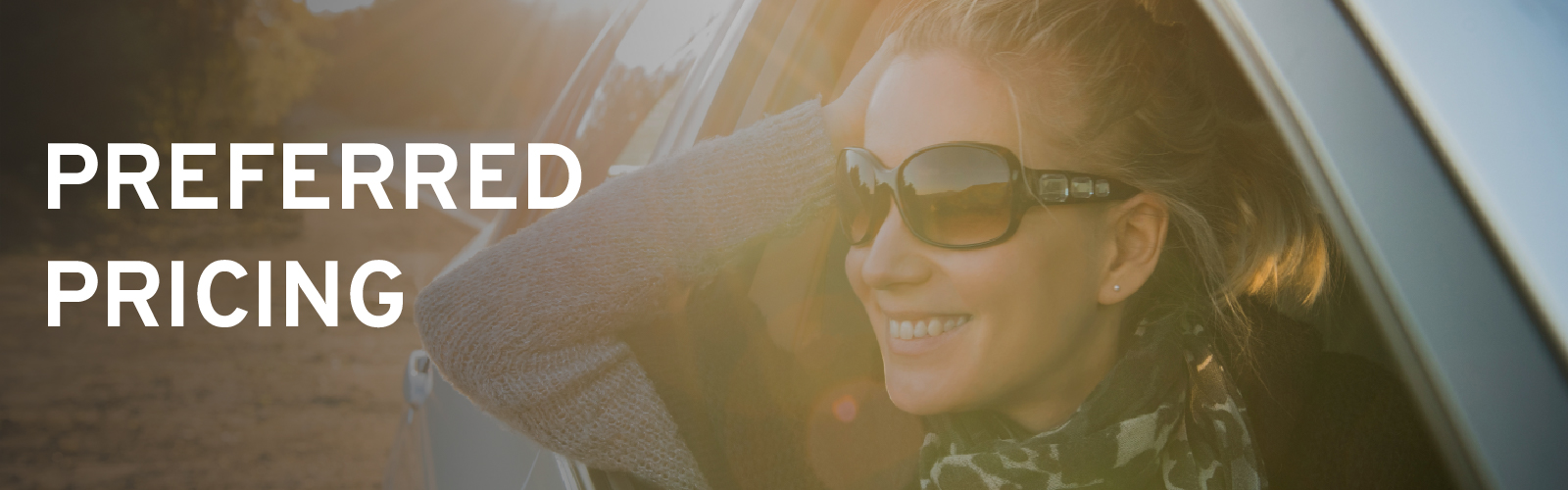 Smiling woman in car with sunglasses, text "Preferred Pricing" on left side. Sunlight creates lens flare.