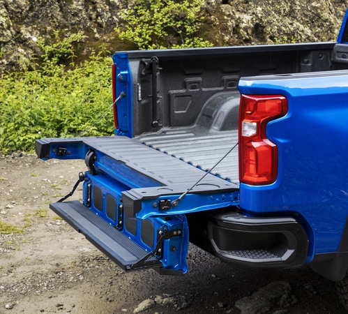 Blue pickup truck with an open tailgate and step feature, parked on a rocky trail.