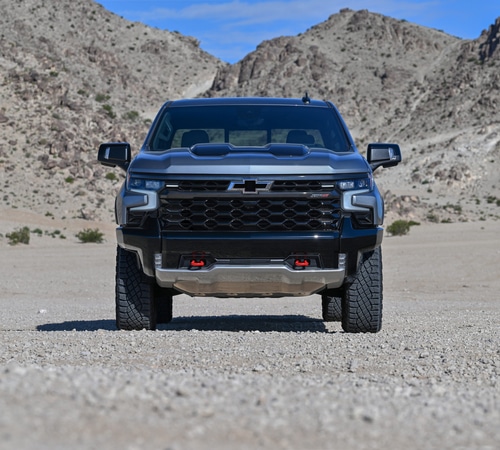A black pickup truck in a desert landscape with rugged mountains in the background.