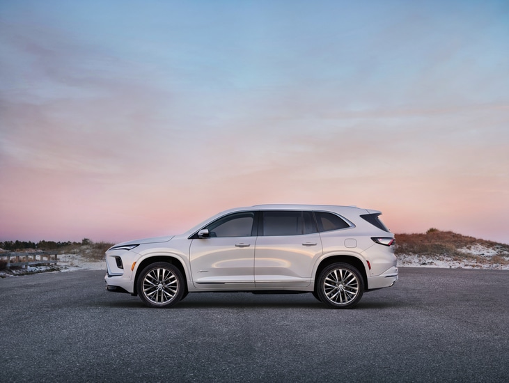 Red SUV with a sleek design parked indoors. The vehicle has prominent headlights and a bold front grille. The setting features a modern and spacious environment with architectural elements in the background.