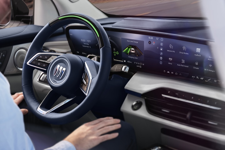 The image shows the interior of a modern car, featuring a steering wheel, a digital dashboard, and a large touchscreen display on the center console. The display shows various controls and settings. The car has a sleek, black design.
