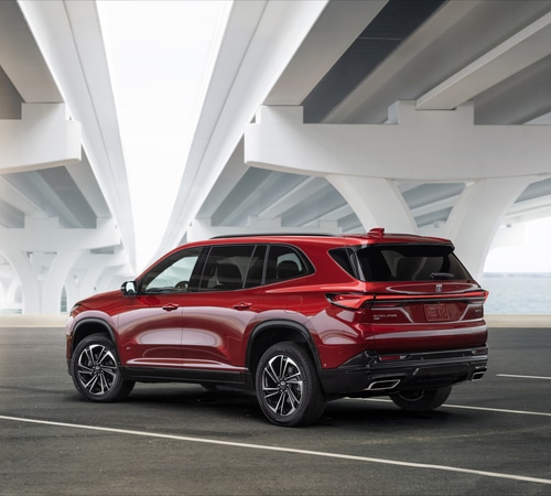 Red SUV parked under a modern bridge, showcasing sleek design and rear features.