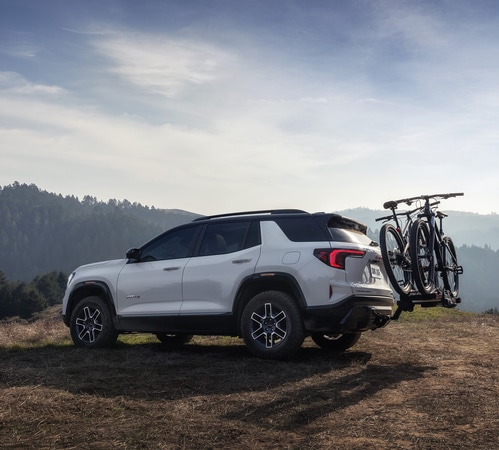 SUV parked on a scenic hill with two bicycles mounted on the rear, under a clear sky.