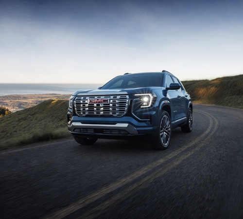 Blue GMC SUV driving on a scenic coastal road with grassy hills and ocean views.