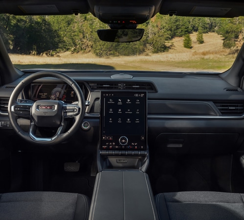 Modern car interior with digital dashboard and touchscreen in a natural, wooded setting.