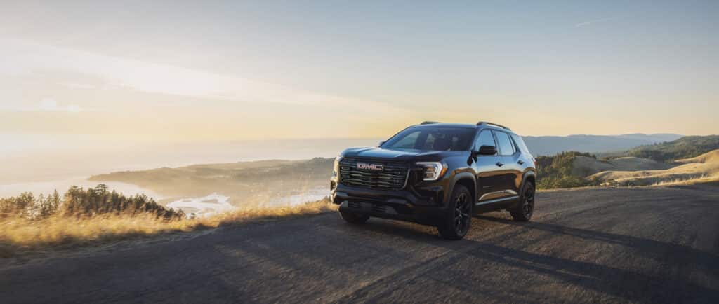 Black SUV on a scenic hillside road at sunset, overlooking rolling hills and a distant coastline.