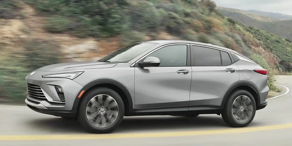 Silver SUV driving on a winding mountain road, surrounded by lush greenery and rocky terrain.