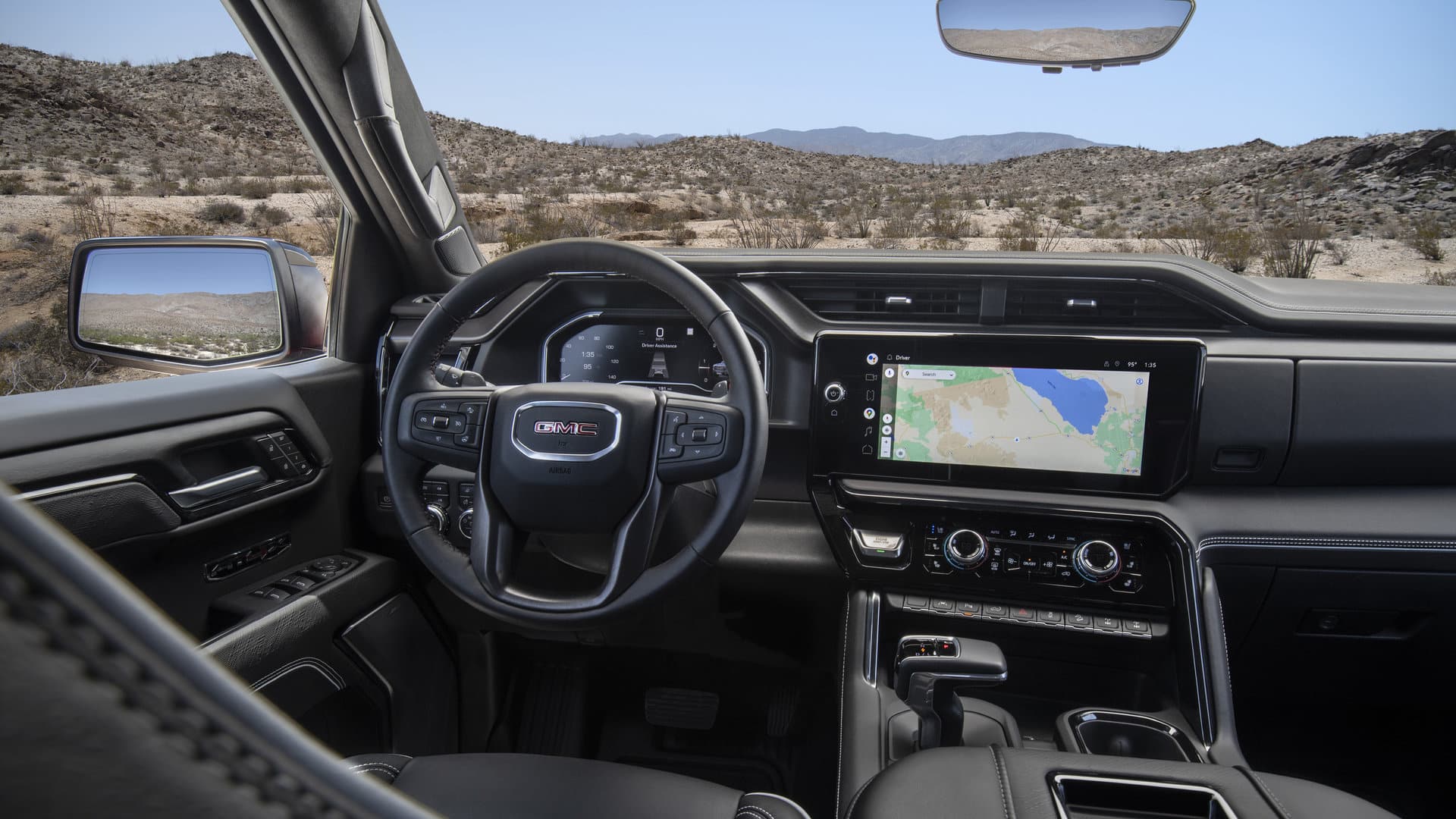 Interior of a GMC vehicle showing the steering wheel, dashboard with navigation screen, and desert view.