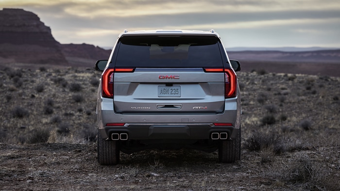 Rear view of a silver GMC Yukon AT4 SUV parked on a desert landscape at dusk.