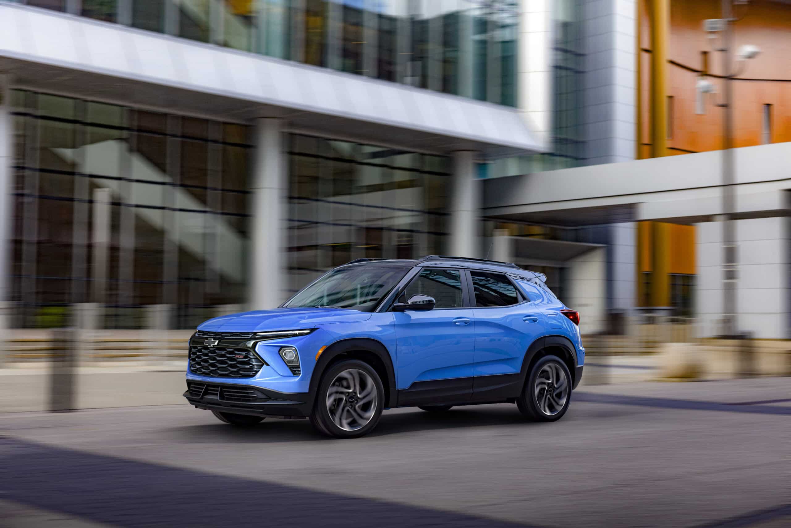 Blue SUV driving past modern glass buildings in an urban setting.