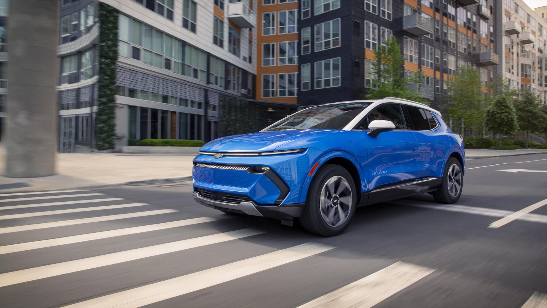 Blue SUV driving on city street with modern buildings in the background.