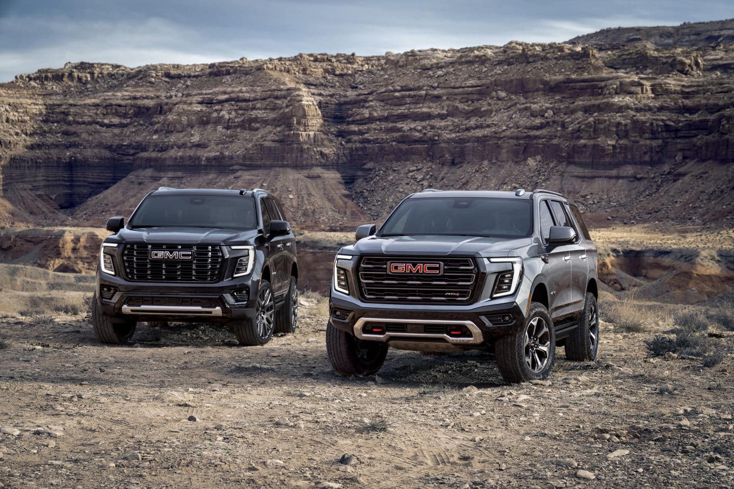Two GMC SUVs parked on rugged terrain with a scenic canyon backdrop.