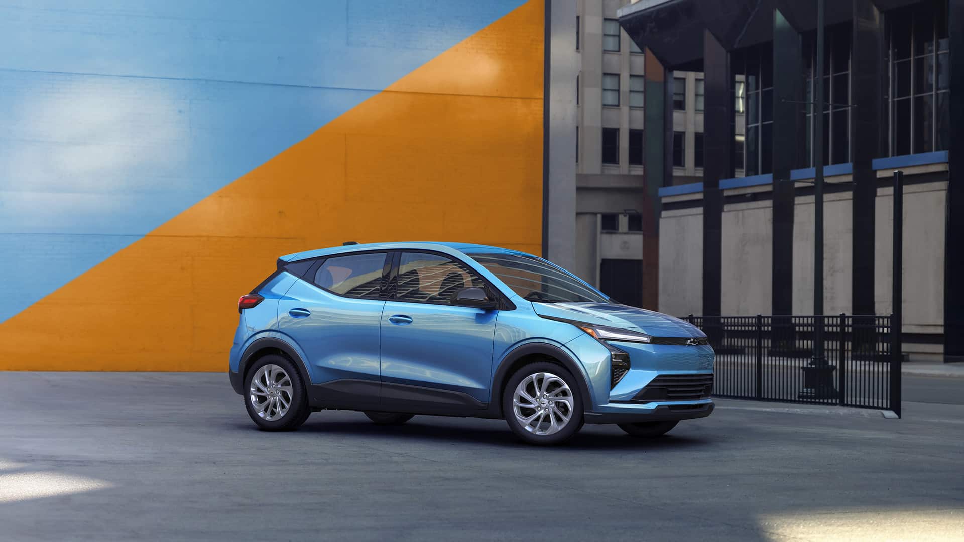 Blue electric car parked in an urban setting with a vibrant blue and orange wall backdrop.