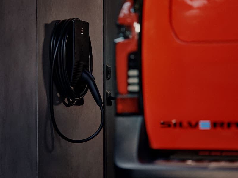 Electric vehicle charging station with cable beside a red car, emphasizing eco-friendly transportation.