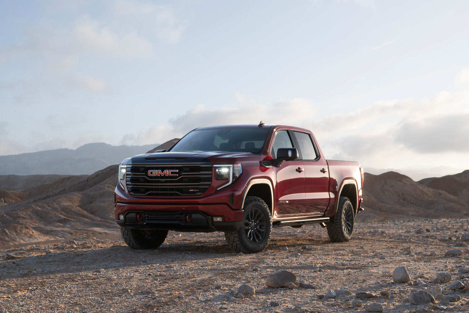 Red GMC truck parked on rocky terrain with mountains in the background under a cloudy sky.