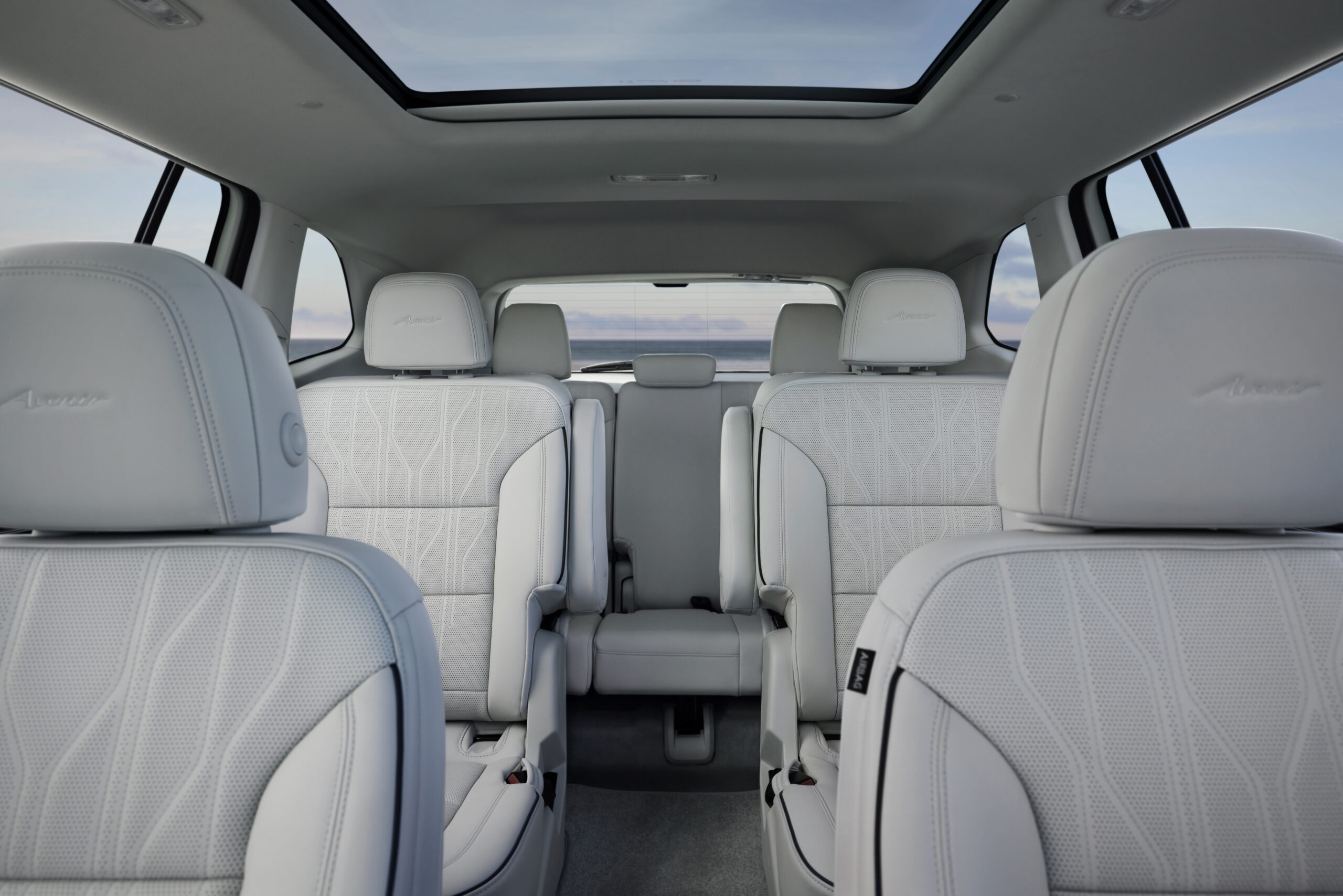 Luxurious car interior with white leather seats and a panoramic sunroof.