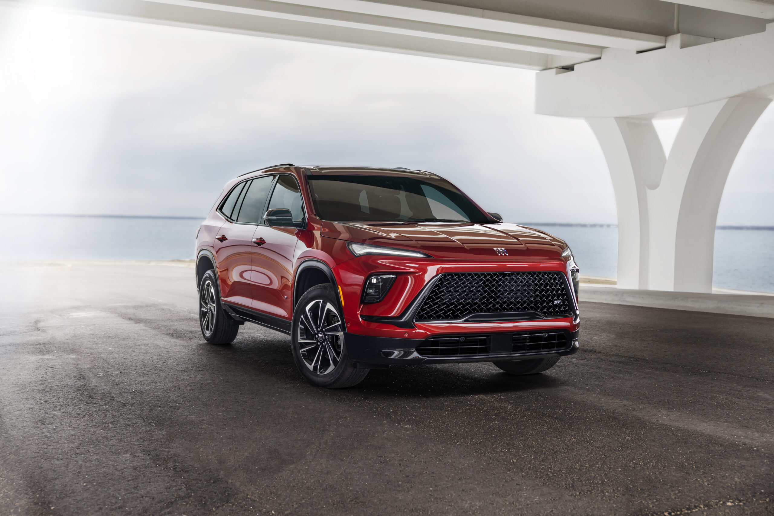 Red SUV parked under a modern structure near a body of water, showcasing sleek design and sporty features.