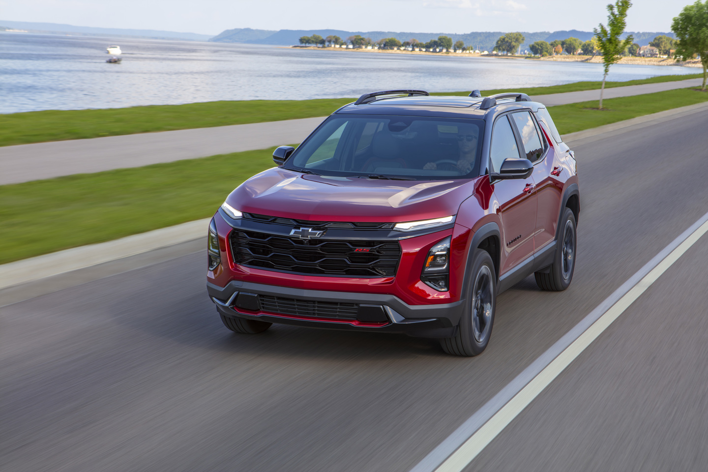 Red Chevrolet SUV driving on a scenic lakeside road with clear skies.