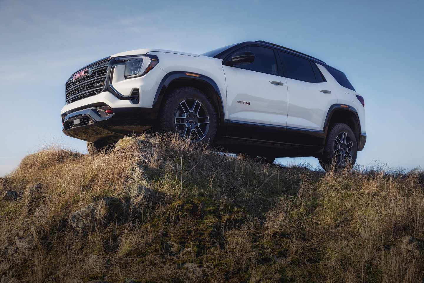 White SUV on a grassy hill under a clear blue sky, showcasing its off-road capability.