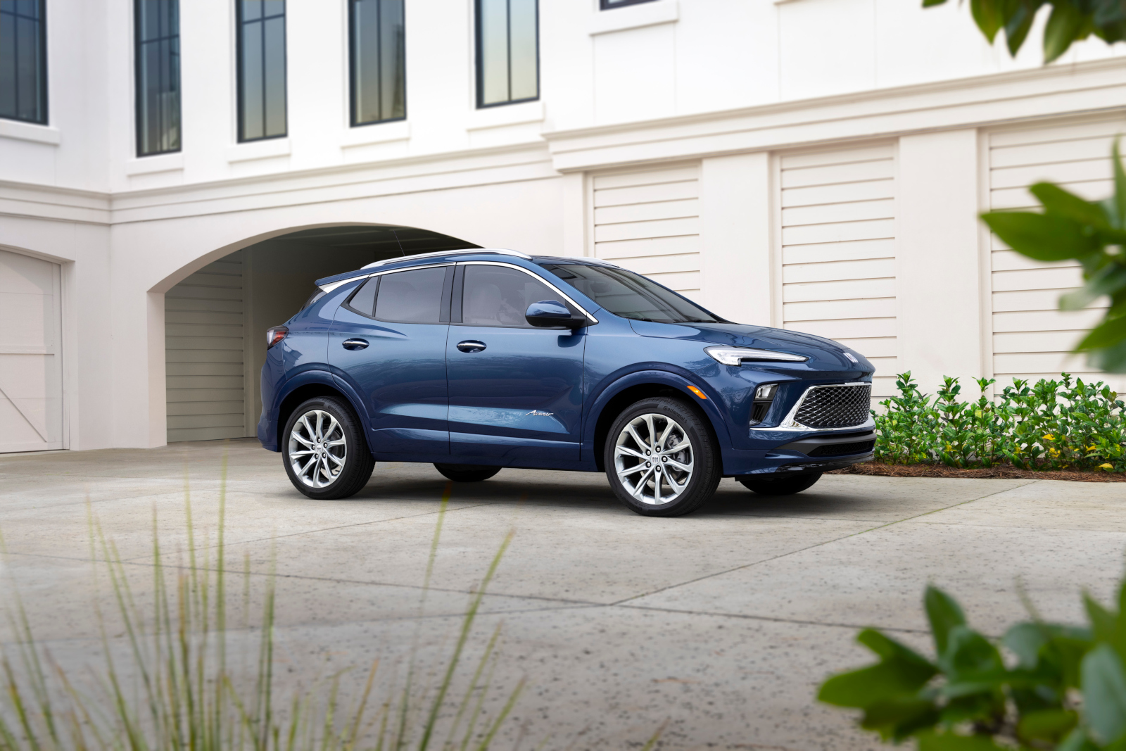Blue SUV parked in front of a modern white building with large windows and lush greenery.